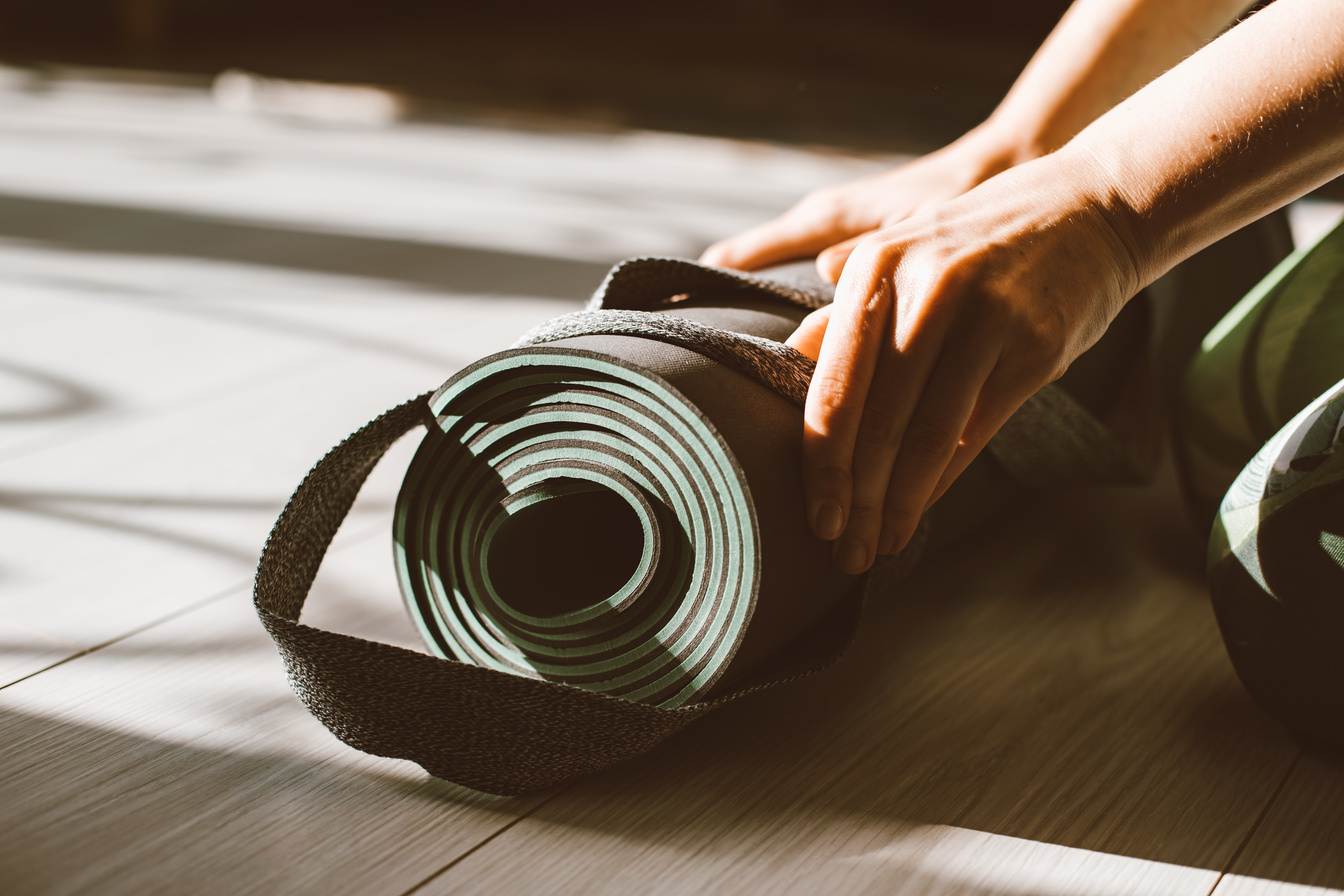 A Person Holding a Yoga Mat with a Strap on the Floor